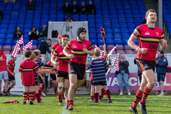 Rugby players high-fiving kids and running onto the pitch